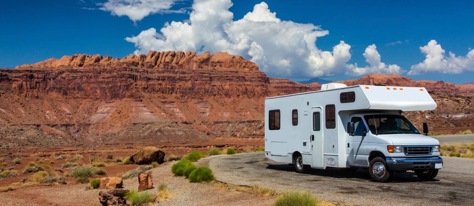 White RV or camper with red cliffs and blue sky behind it